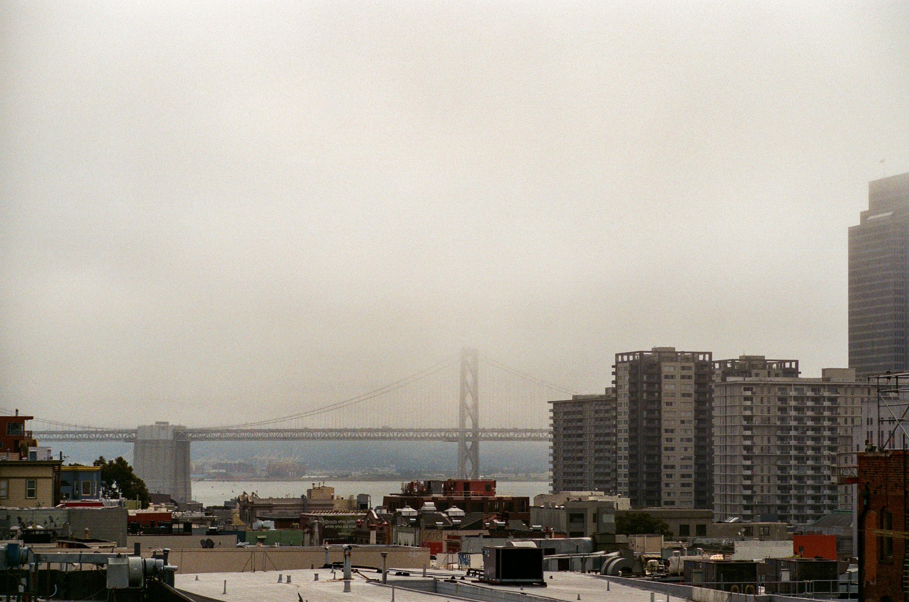 Foggy view of the Golden Gate Bridge partially obscured by mist, with city buildings in the foreground under an overcast sky.