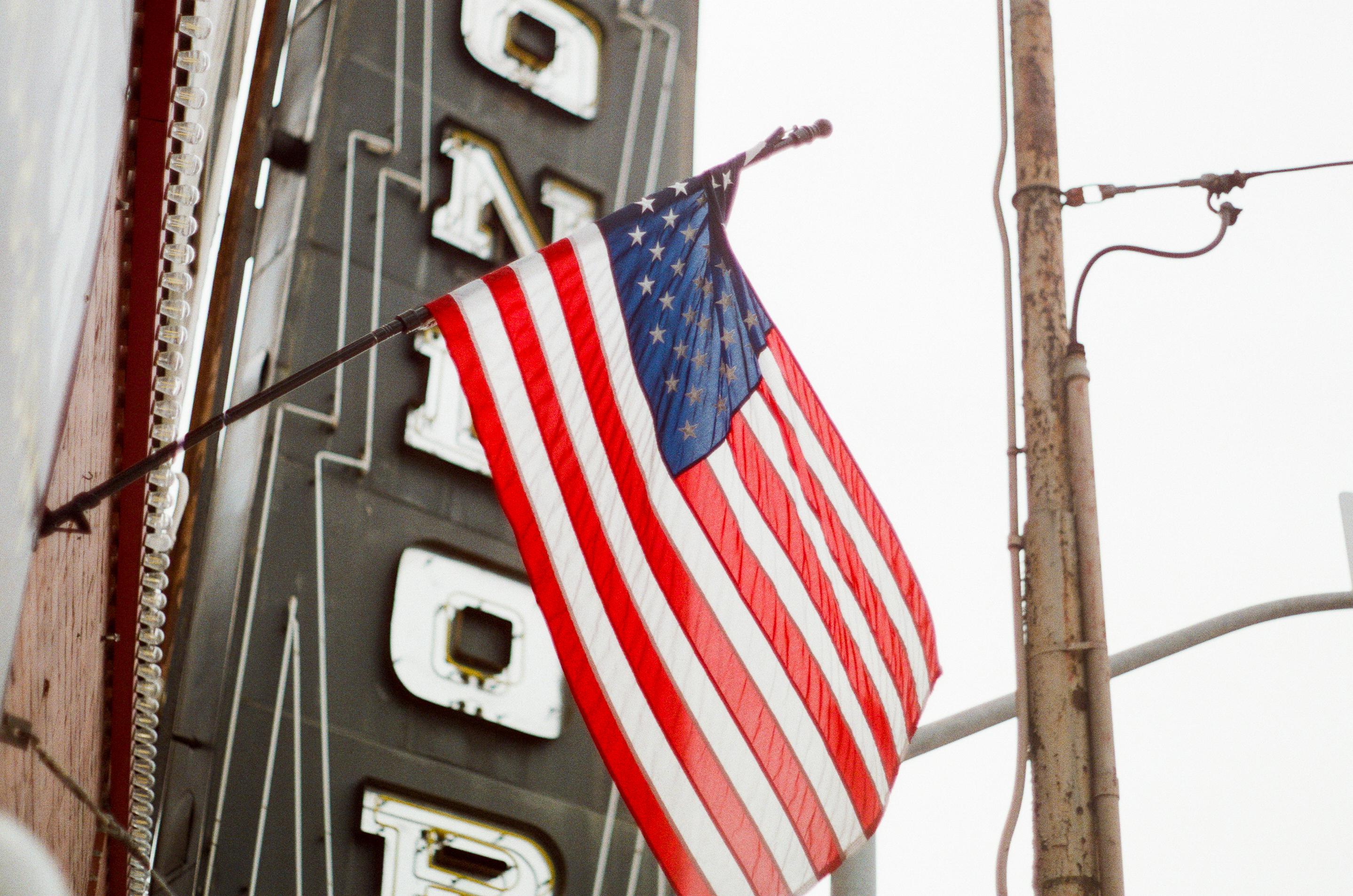 American flag waving in front of a vintage theater marquee with the word "HONOR" partially visible.