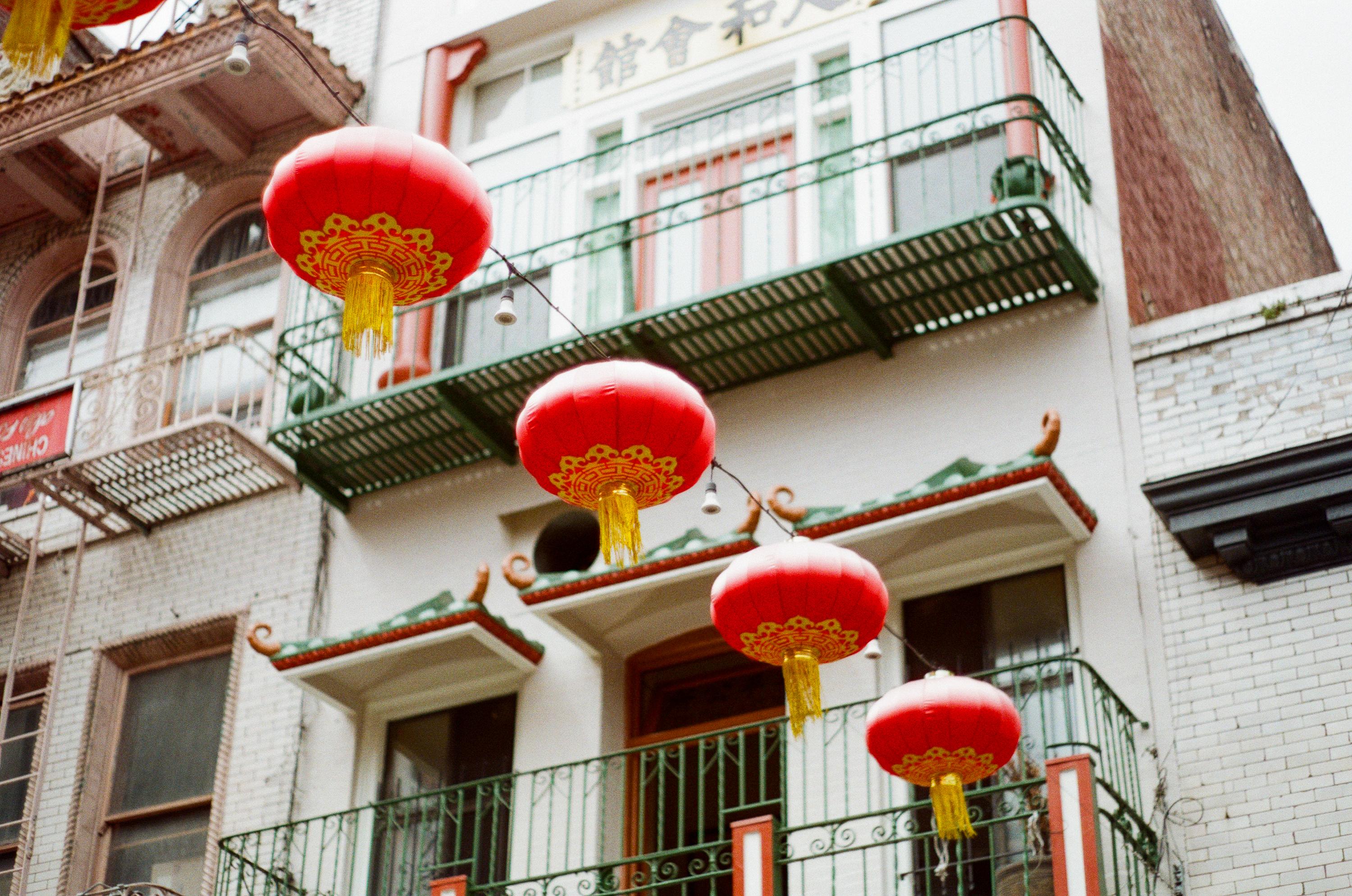 Red Chinese lanterns hanging in front of a building with balconies and traditional architectural details.