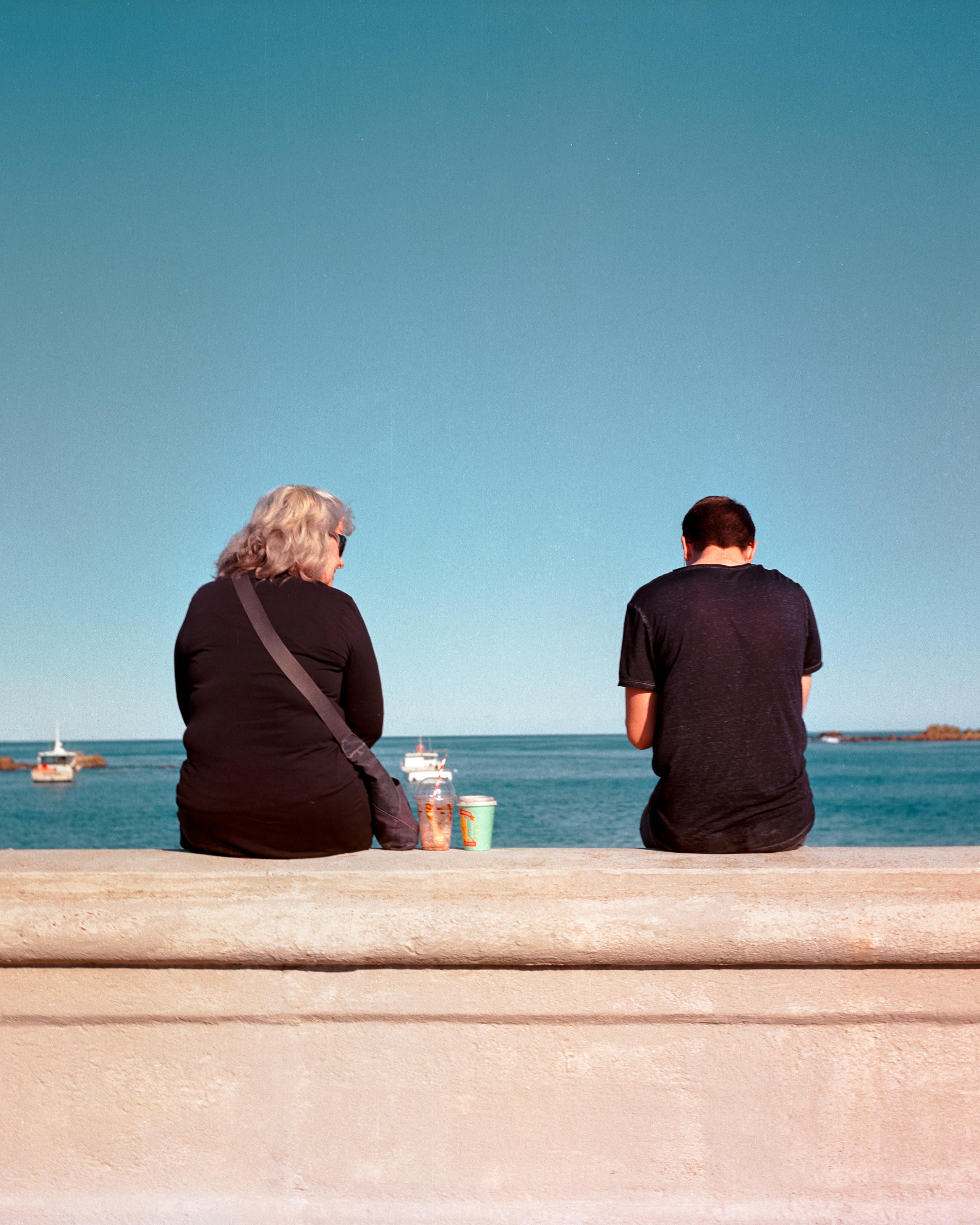 Photo of two people sitting on a sea wall 