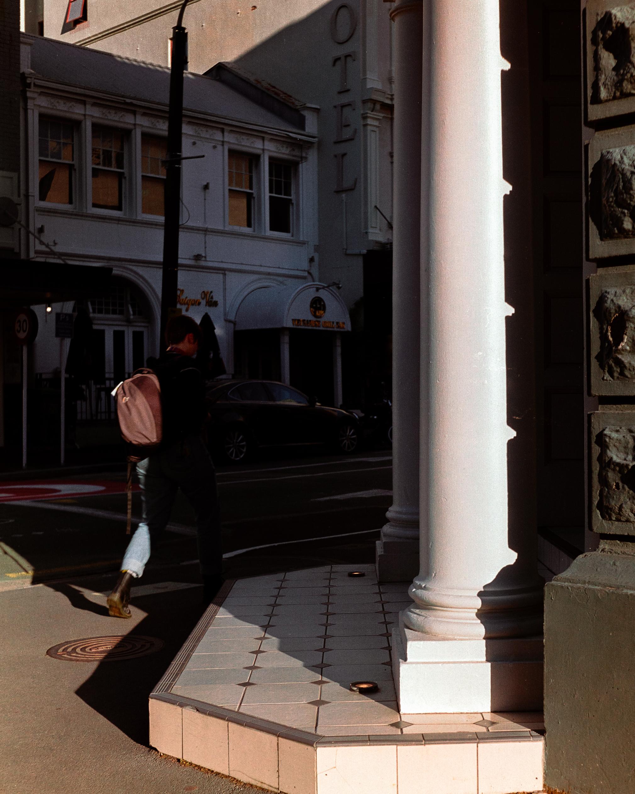 Photo of a woman walking into shadow on a street corner 